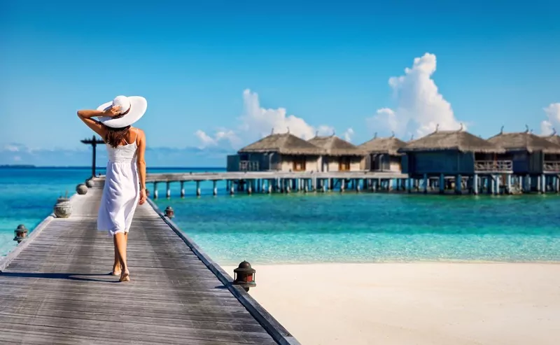 Woman in white walking over a wooden jetty in the Maldives
